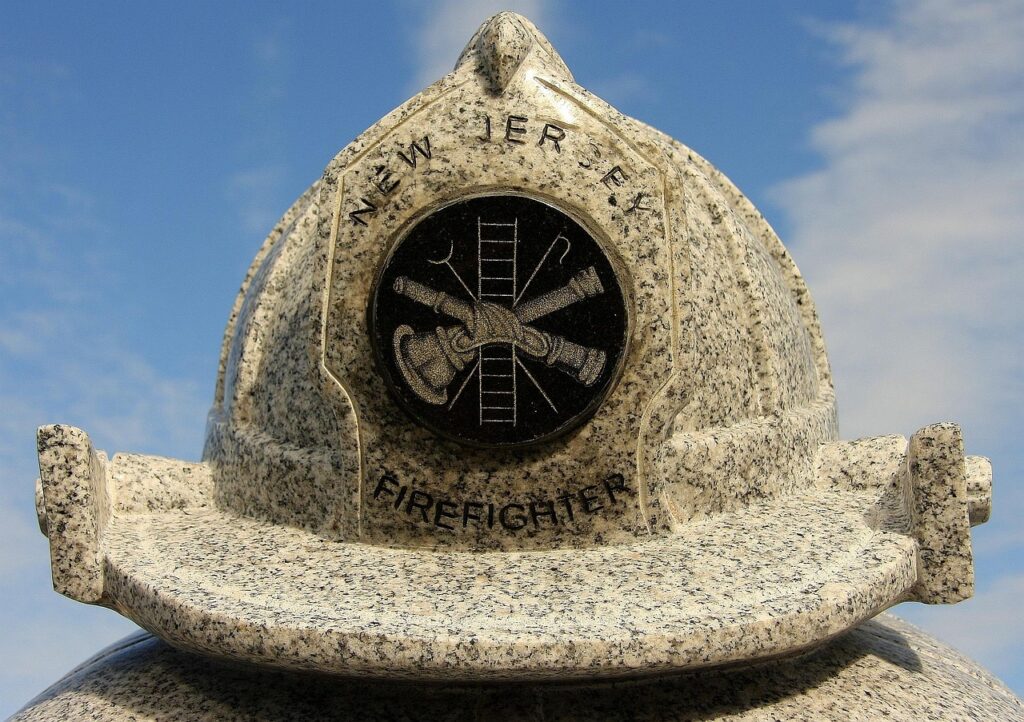 Granite firefighter helmet monument engraved with “New Jersey Firefighter” under a blue sky.