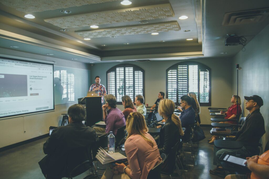Speaker presenting to a group of professionals seated in a training room with a projected screen.