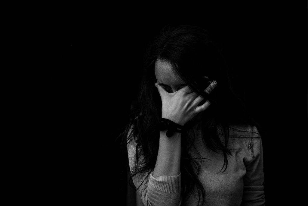 Woman in emotional distress covering her face with her hand in a dark setting.