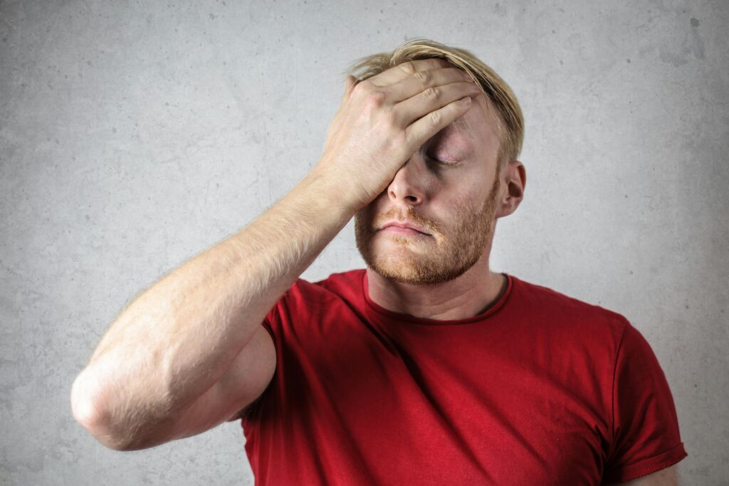 Stressed man in a red shirt holding his forehead with his eyes closed.