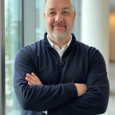 Ted Adams, founder of The Alarm Room, standing confidently with arms crossed near office windows.