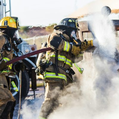 Firefighters extinguishing a live vehicle fire using hose lines during fireground operations.