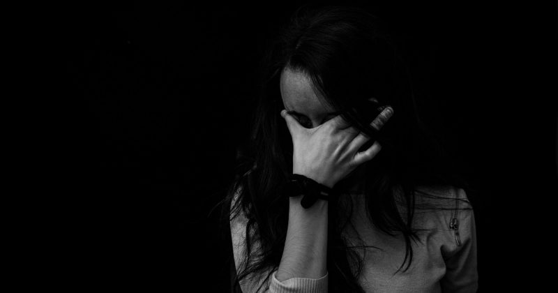 Woman in emotional distress covering her face with her hand in a dark setting.