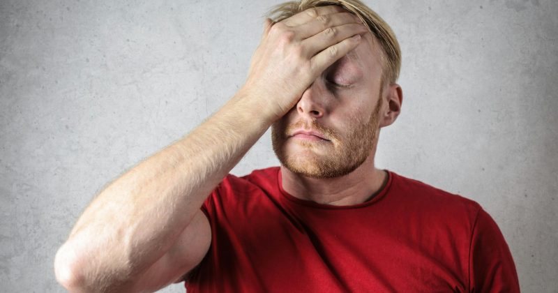 Stressed man in a red shirt holding his forehead with his eyes closed.