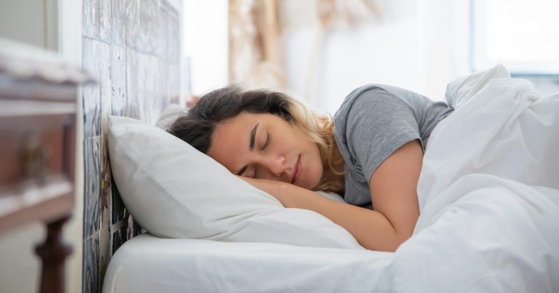 Young woman sleeping peacefully in bed with white sheets and a soft pillow.